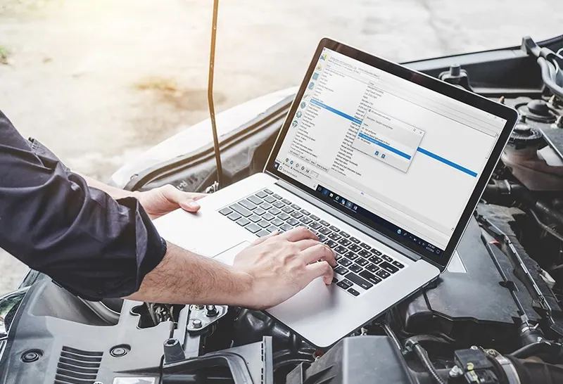 A laptop and J2534 pass-thru device connected to a vehicle's OBD2 port for ECM programming.