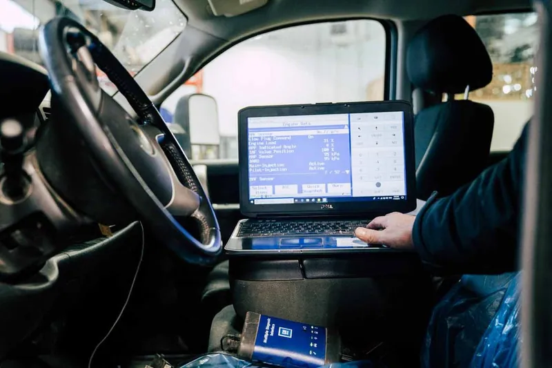 A diagnostic laptop and J2534 pass-through device connected to a vehicle's OBD2 port for ECM programming.