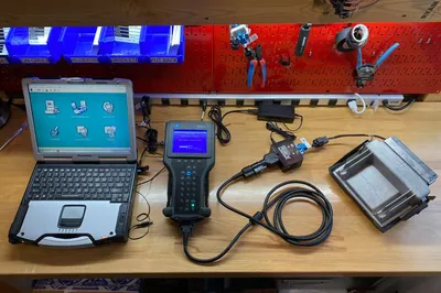A mechanic using a laptop and a J2534 pass-through device to program a vehicle's Engine Control Module.