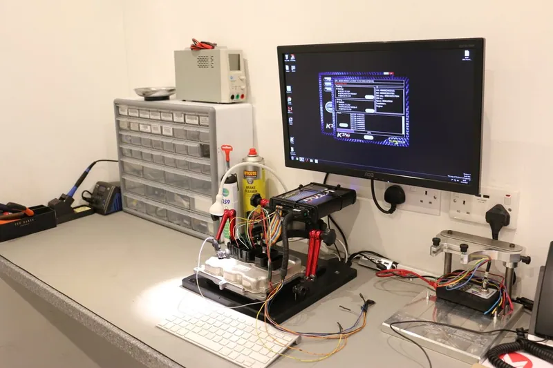 An Engine Control Module connected to a bench programming harness with various colored wires for data transfer and immobilizer syncing.