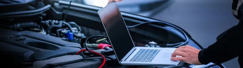 A mechanic using a laptop and a pass-thru device to reprogram a vehicle's Engine Control Module.