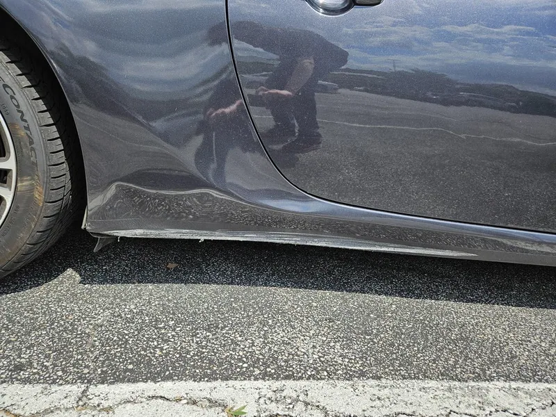 A damaged rocker panel on a Lexus IS pulling away from the vehicle body due to broken clips.
