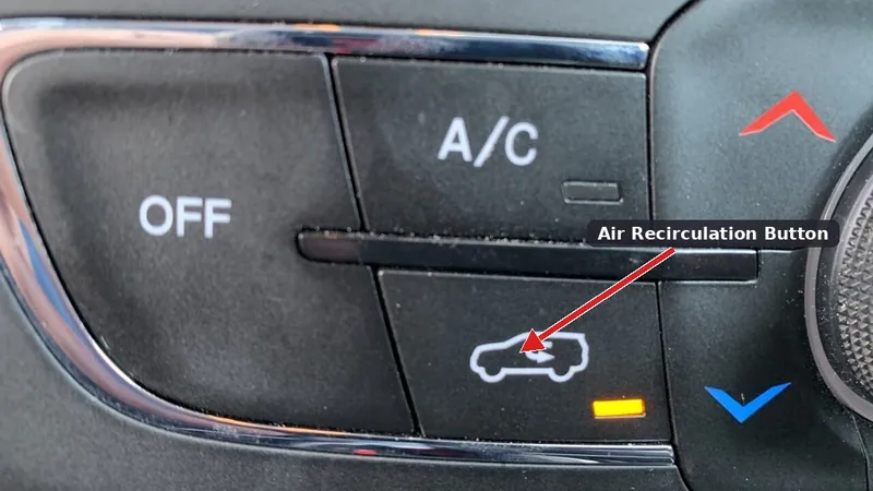 A close-up of a car's climate control panel focusing on the air recirculation button.