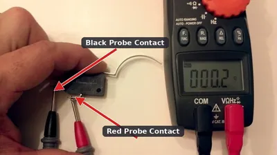 A mechanic using a digital multimeter to test the electrical continuity of a trunk latch microswitch.