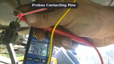 A mechanic using a digital multimeter to test the electrical pins on an A/C pressure sensor connector.