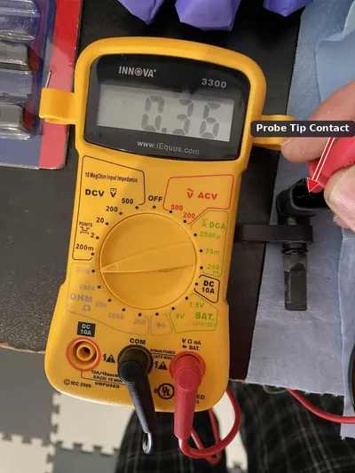 A mechanic using a digital multimeter to test the electrical resistance of an ABS wheel speed sensor.