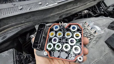 A technician removing or installing an ABS pump and control module assembly in a vehicle engine bay.