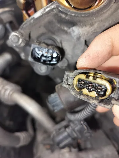 A damaged and oil-soaked camshaft position sensor connector showing brittle, cracked plastic.