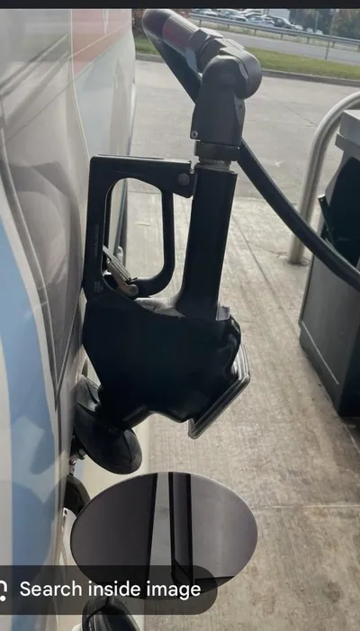 A gas station pump nozzle inserted into a vehicle's fuel filler neck.
