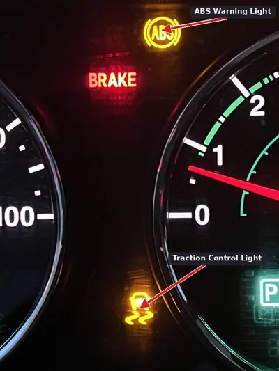 A vehicle dashboard showing the ABS, Traction Control, and Check Engine lights illuminated, with the speedometer at zero.