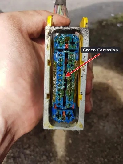 A disconnected automotive electrical connector showing heavy green corrosion on the metal pins.
