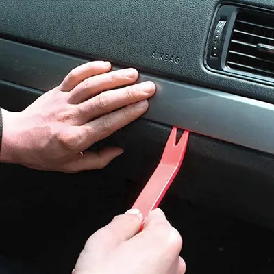 A mechanic using a plastic pry tool to carefully remove interior center console trim panels.