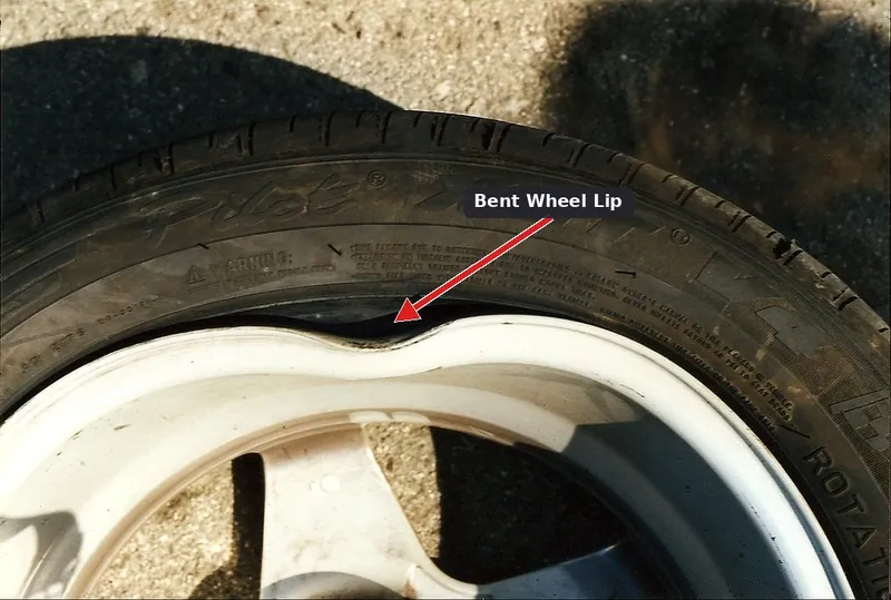 An alloy wheel with a visible bend and dent on the inner lip from pothole damage.