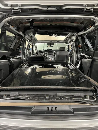 The interior of a Kia Telluride with the headliner completely removed, exposing the bare metal roof and the large panoramic sunroof cassette.