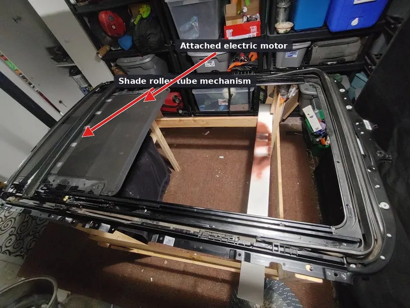 A complete, uninstalled panoramic sunroof cassette assembly resting on a workbench, showing the tracks, motor, and shade roller.